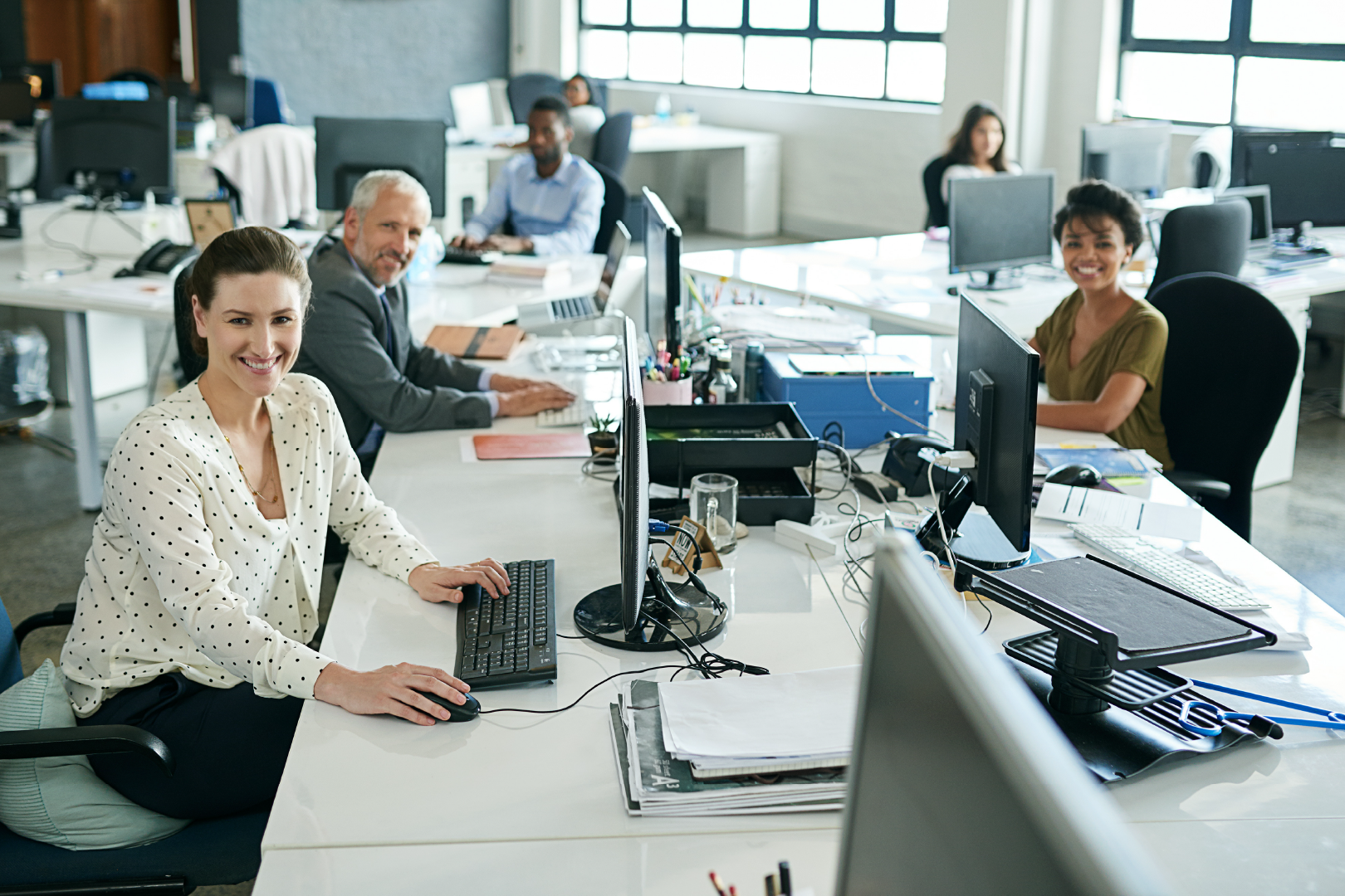 Team sitting at their desks in an office and smiling at the camera